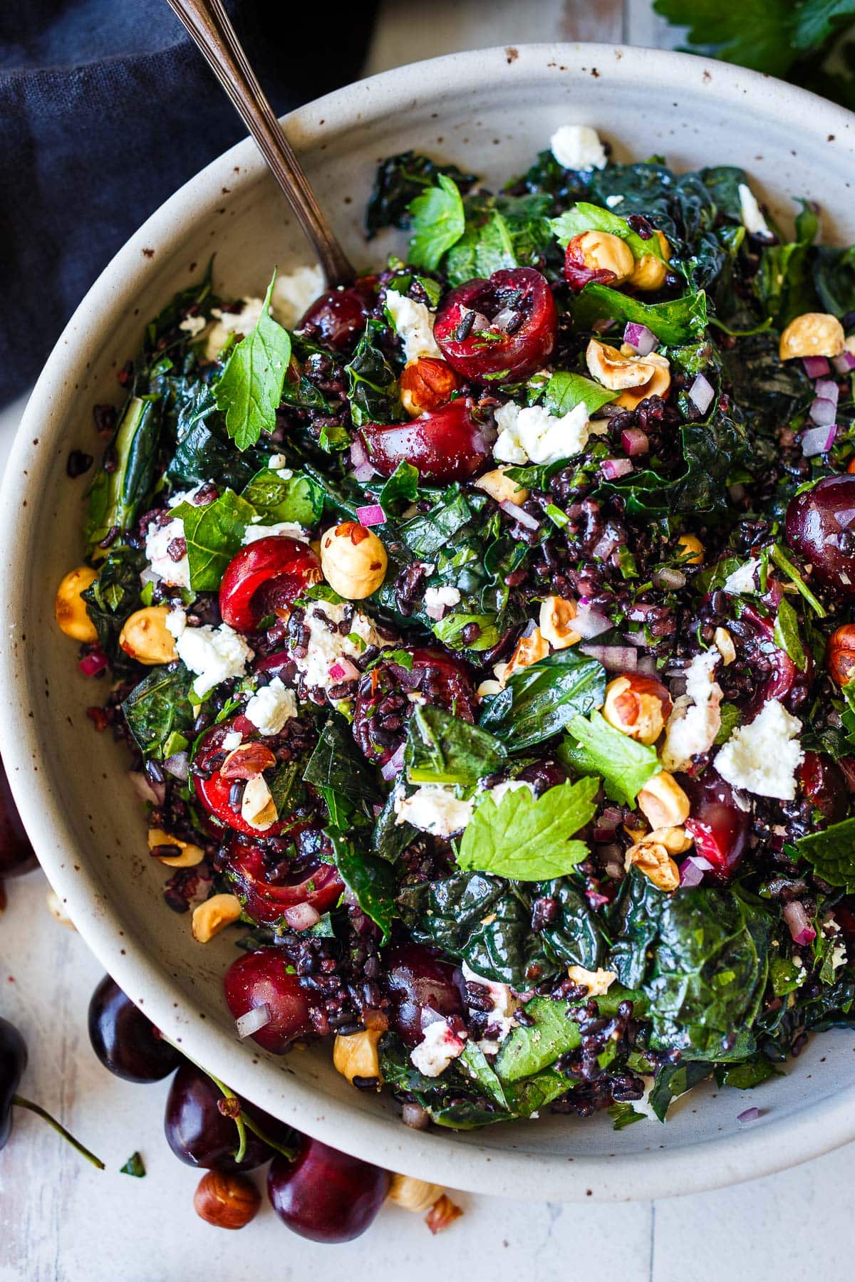 large bowl with cherry salad with kale and black rice, served with toasted hazelnuts, parsley, and goat cheese.