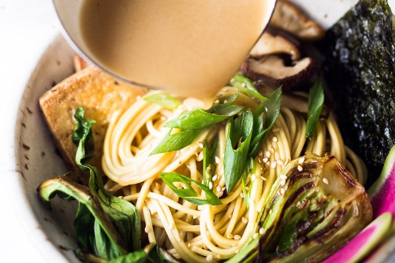 Pouring miso broth over a bowl of noodles, veggies and tofu.
