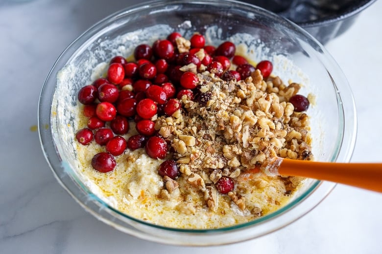 combining wet and dry ingredients for cranberry cake in a glass bowl - batter with fresh cranberries and toasted, crushed walnuts on top.