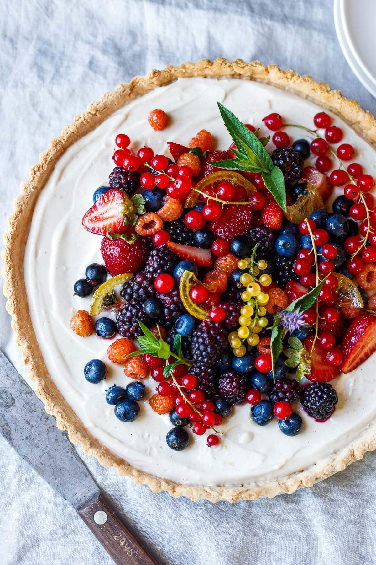 vegan berry tart topped with an assortment of colorful berries and fresh herbs.