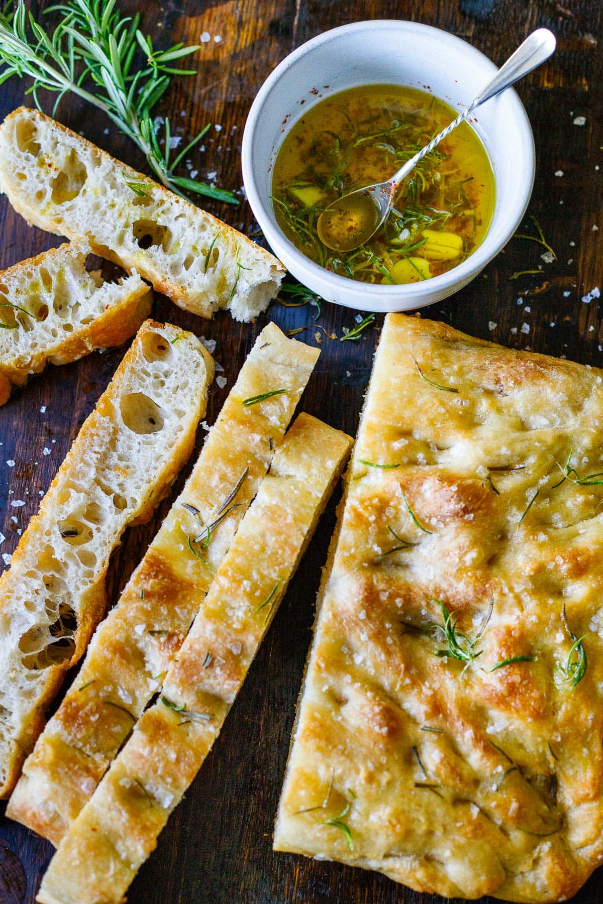 focaccia bread loaf with thin slices cut off next to small bowl of garlic rosemary dipping oil.