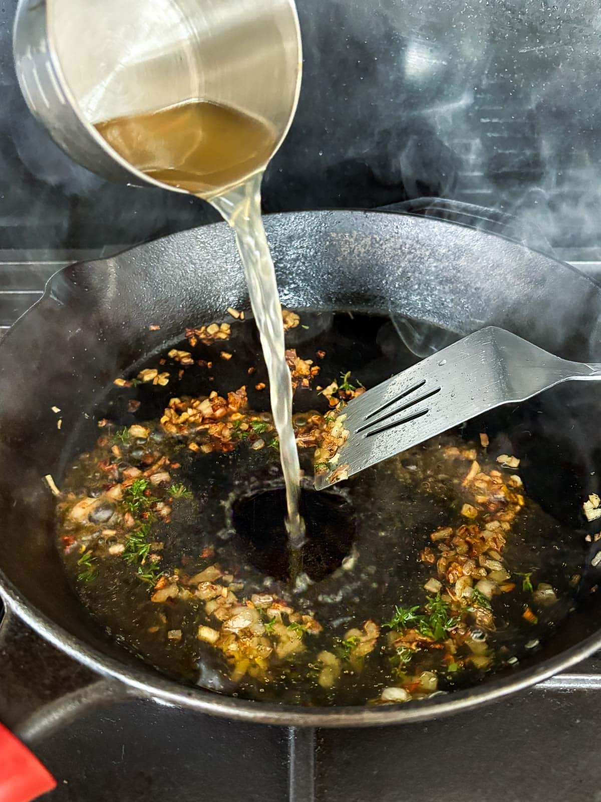 pouring white wine into a cast iron skillet to make pan sauce - skillet has browned bits and parsley with a metal spatula.